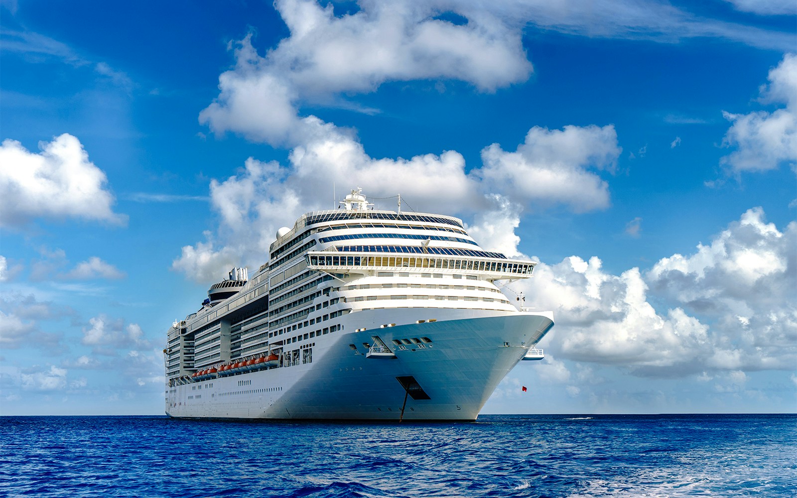 Cruise ship sailing in crystal blue waters near a rocky coastline.