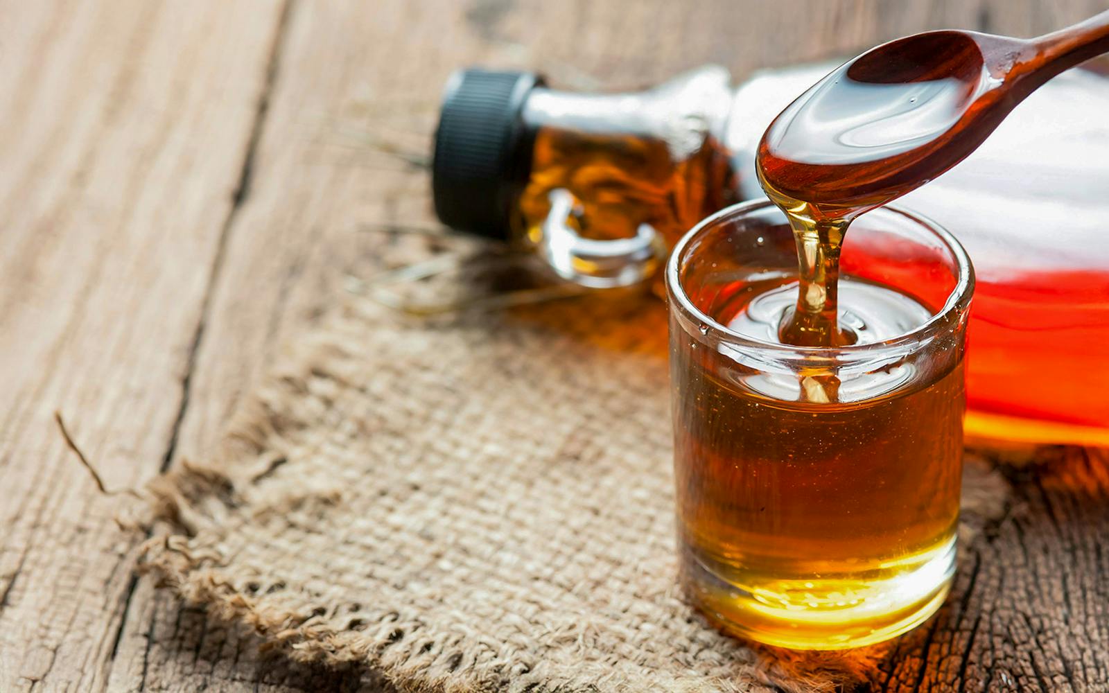 Pouring maple syrup from glass bottle into a glass on wooden table.