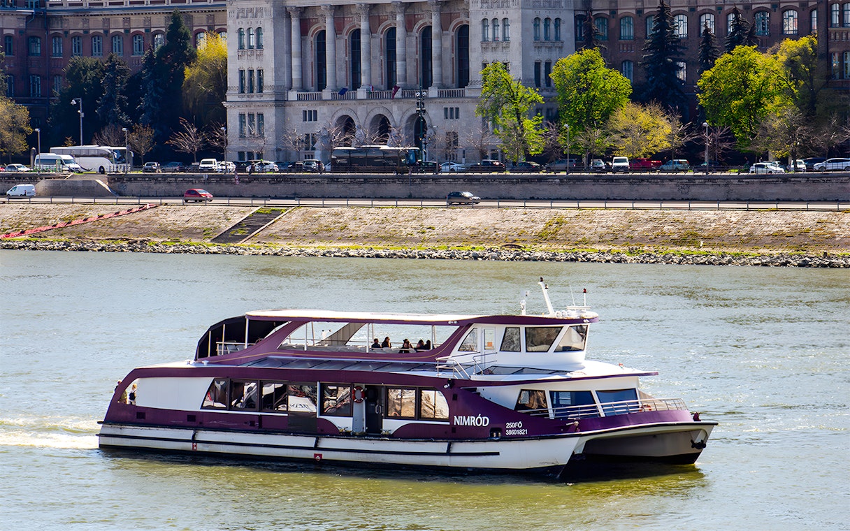 Danube cruise boat with passengers near Budapest riverside.