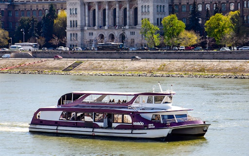 Danube cruise boat with passengers near Budapest riverside.