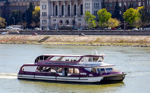 Danube cruise boat with passengers near Budapest riverside.