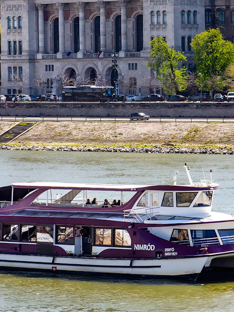Danube cruise boat with passengers near Budapest riverside.