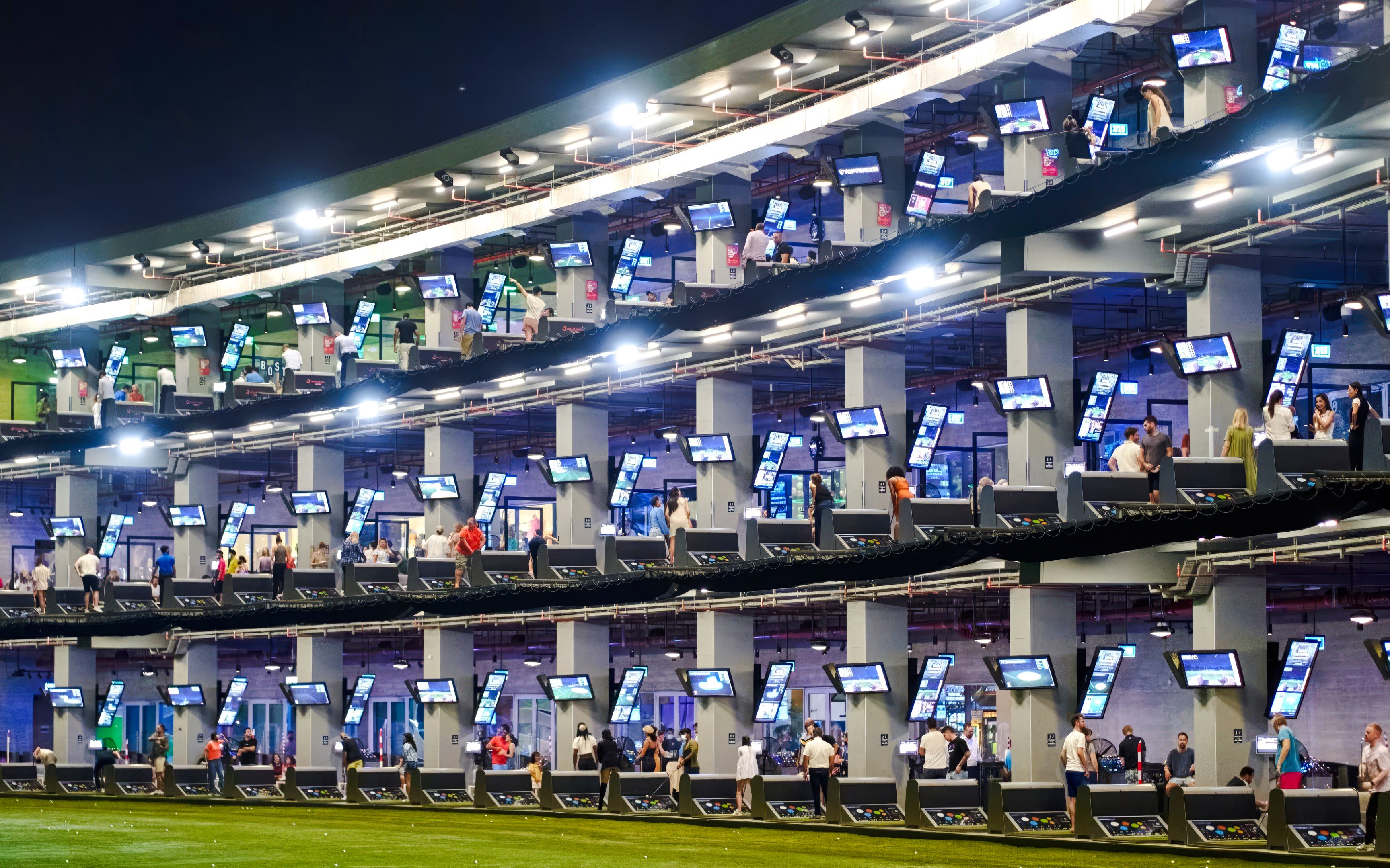 Golfers at multi-level driving range, Topgolf Dubai, enjoying night practice.