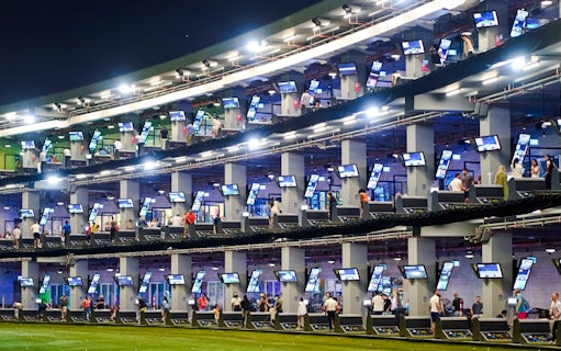 Golfers at multi-level driving range, Topgolf Dubai, enjoying night practice.