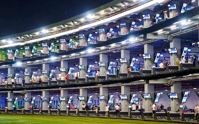 Golfers at multi-level driving range, Topgolf Dubai, enjoying night practice.