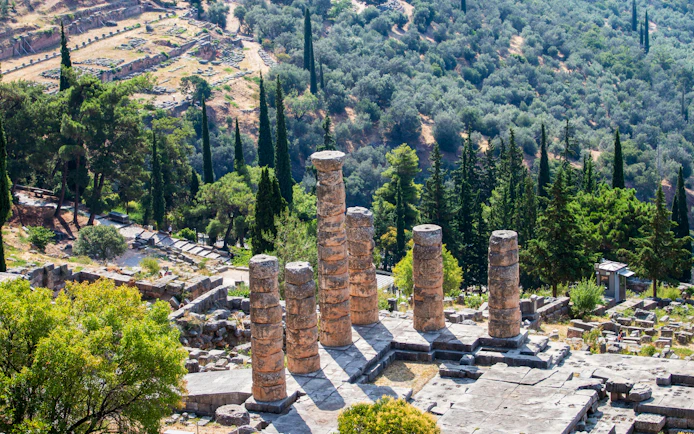 Ruins of Apollo Temple in Delphi, Greece surrounded by lush greenery.