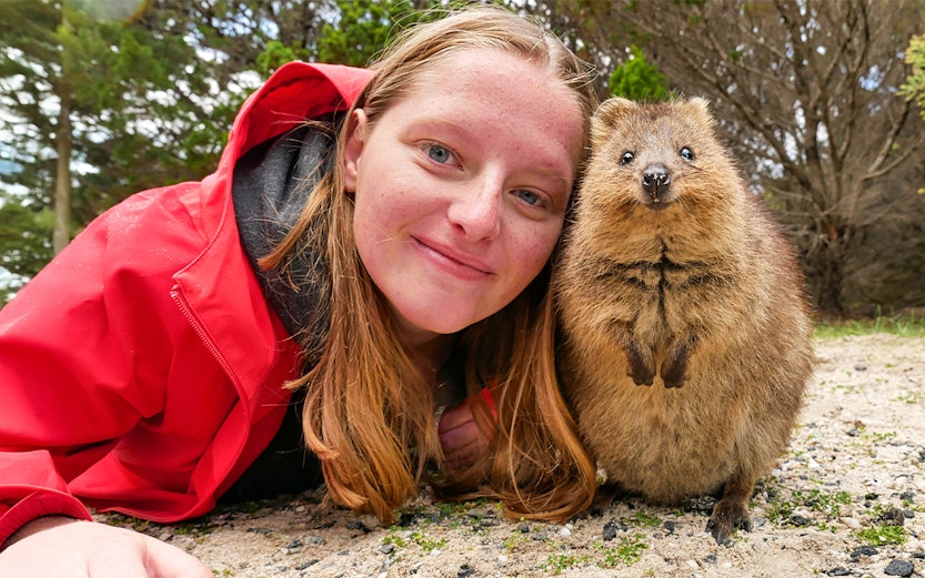 Person smiling with a quokka on Rottnest Island during a ferry and adventure boat tour.