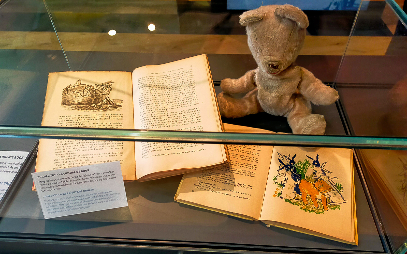 Burned toy and children's books displayed at D-Day Normandy museum exhibit.