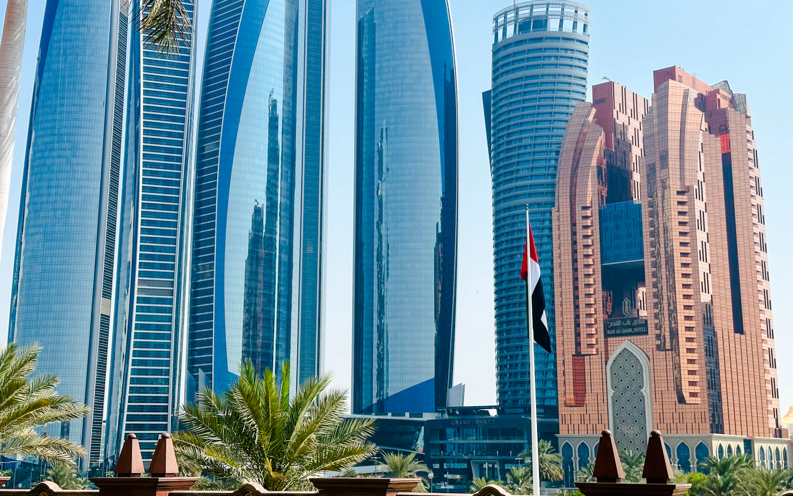 Skyscrapers of Etihad Towers and Bab Al Qasr Hotel in Abu Dhabi with UAE flag in foreground.