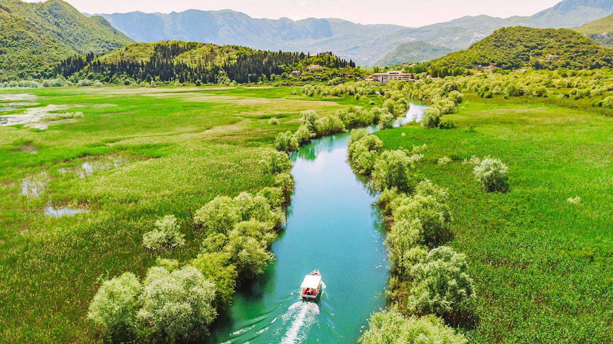 Aerial view of a boat navigating a river through lush greenery on Lake Skadar, Montenegro.