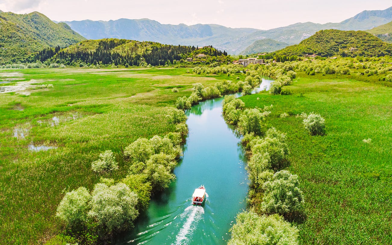 Aerial view of a boat navigating a river through lush greenery on Lake Skadar, Montenegro.