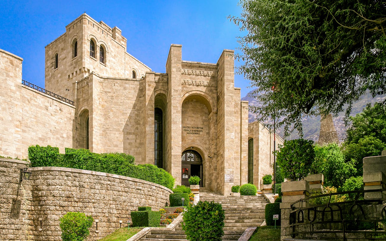 Skanderbeg Museum entrance at Kruje Castle, Albania, with stone architecture and lush greenery.
