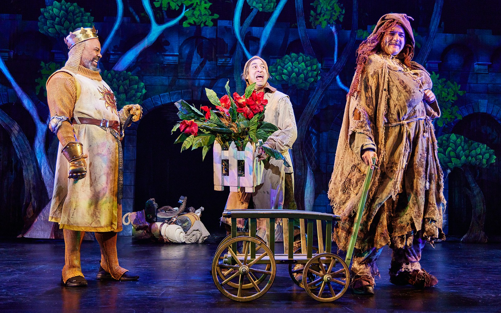 Characters in medieval costumes performing a scene from Spamalot on stage.