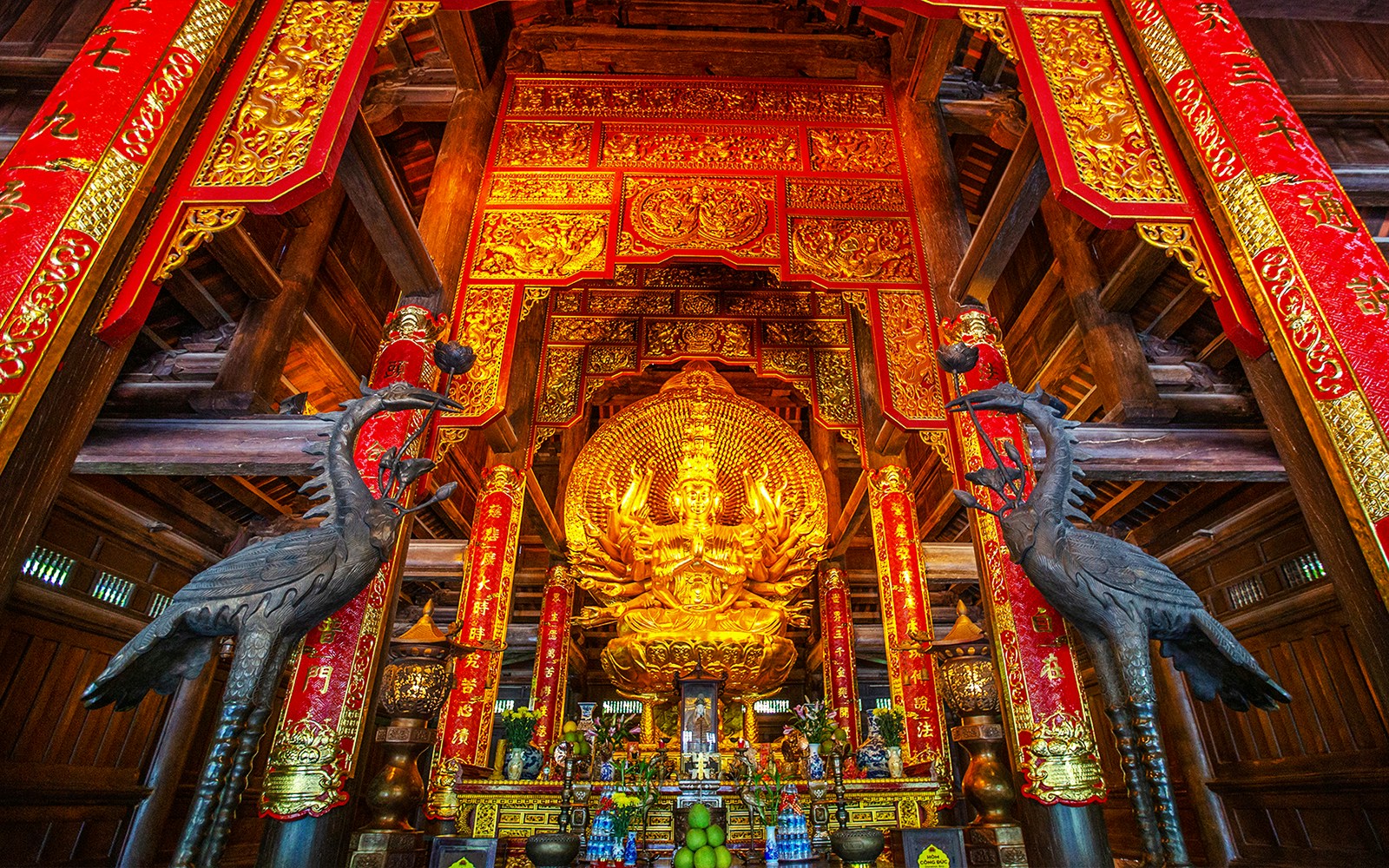 Golden statue and ornate red banners inside Bai Dinh Pagoda complex, Ninh Binh, Vietnam.