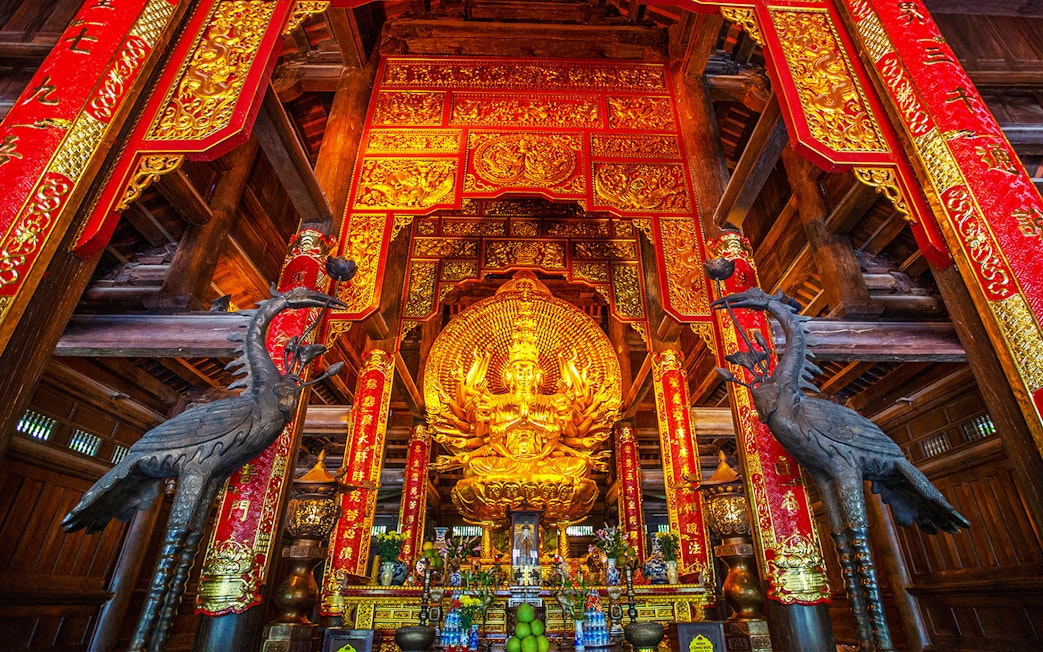 Golden statue and ornate red banners inside Bai Dinh Pagoda complex, Ninh Binh, Vietnam.