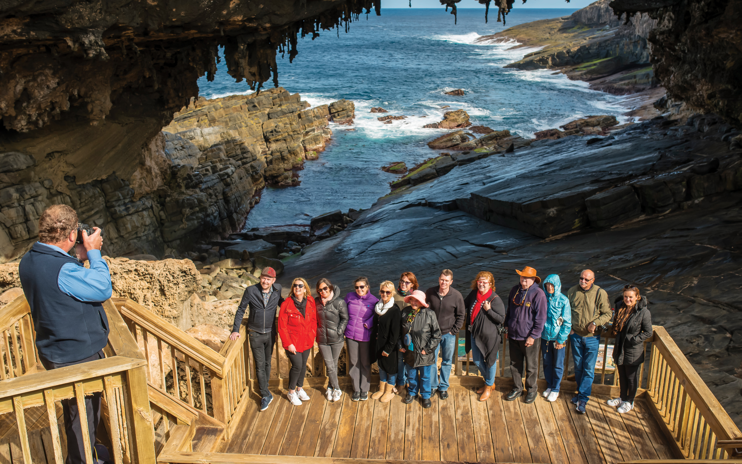 Group posing at Admiral's Arch, Kangaroo Island with ocean and rock formations in the background.