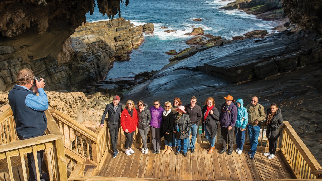 Group posing at Admiral's Arch, Kangaroo Island with ocean and rock formations in the background.
