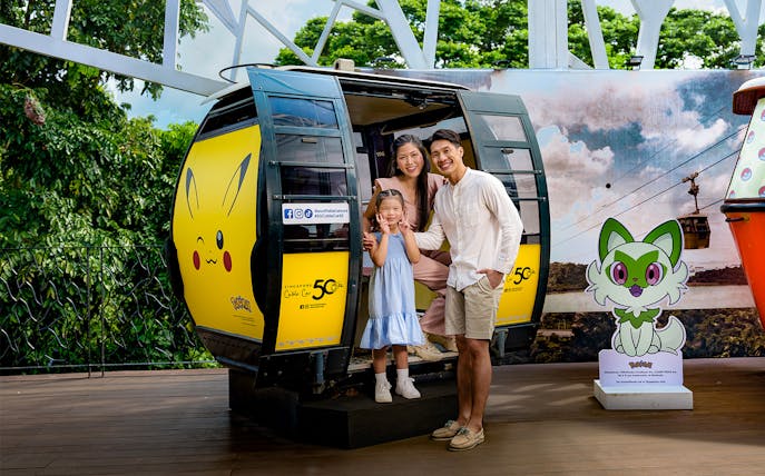 Family posing in front of a Pikachu-themed cable car in Singapore, promoting Arbora Set Lunch.