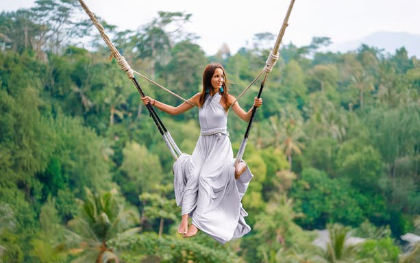 Lady on swing at Alas Harum Bali with lush forest backdrop.