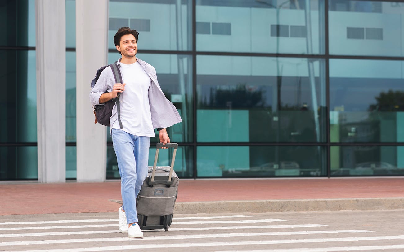 Traveler with luggage walking outside a modern airport terminal.