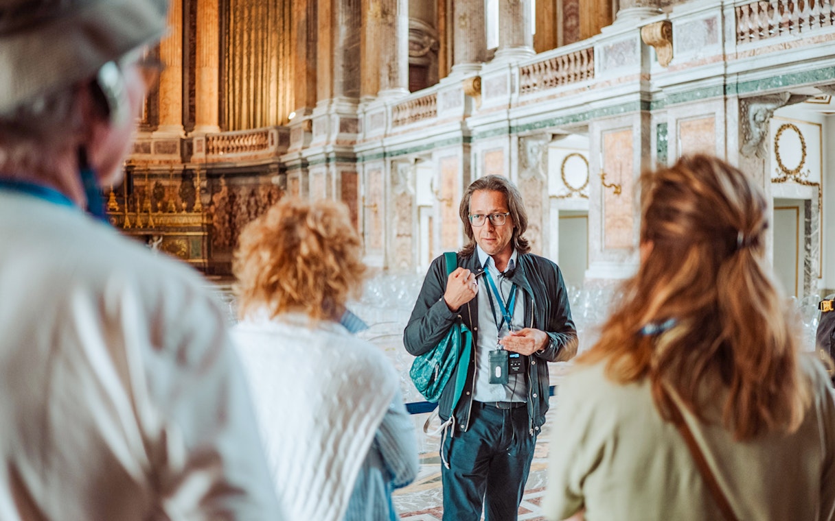 Tour guide leading a group inside the Royal Palace of Caserta, Italy.