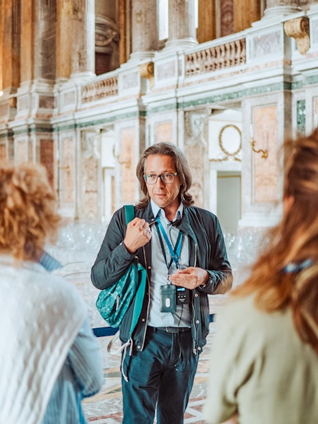 Tour guide leading a group inside the Royal Palace of Caserta, Italy.