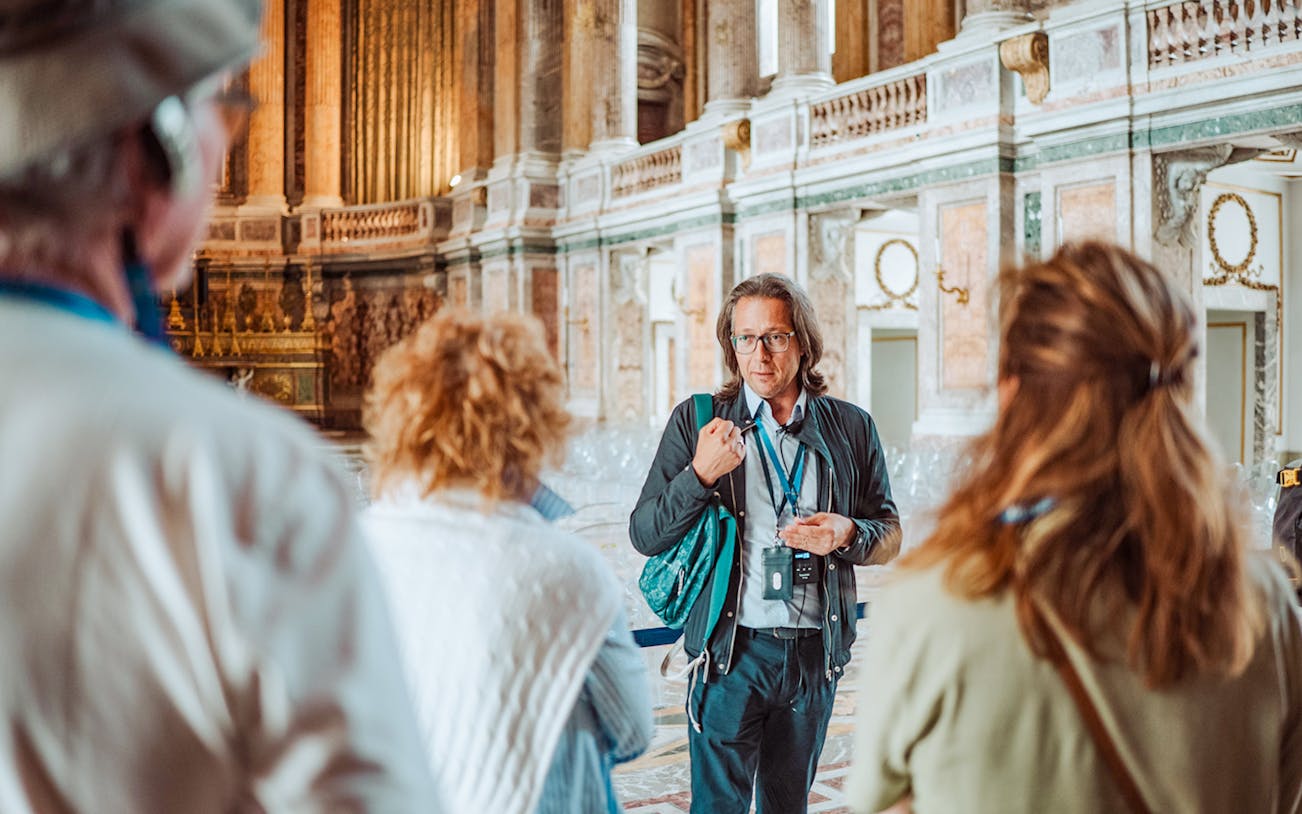 Tour guide leading a group inside the Royal Palace of Caserta, Italy.