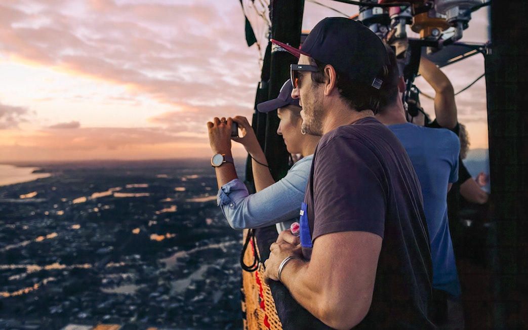 People enjoying a hot air balloon flight at sunset, capturing views over a scenic landscape.