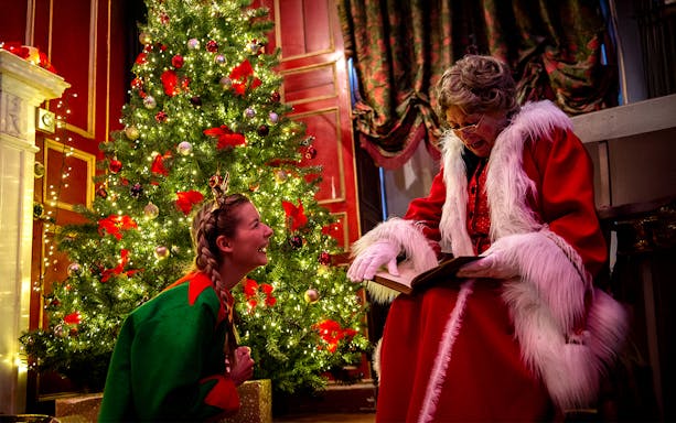 Santa reading to a child by a decorated Christmas tree at Warwick Castle.