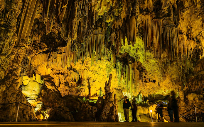 Visitors exploring illuminated stalactites in the Caves of Nerja, Spain.