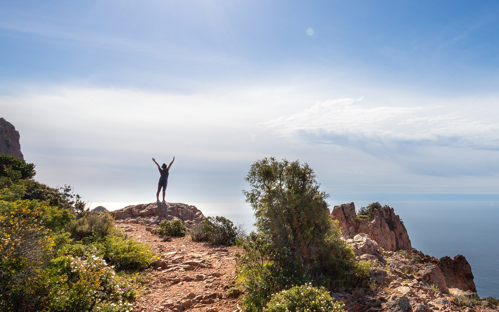 Hiker on rocky cliff overlooking sea at Massif de l'Esterel, France.