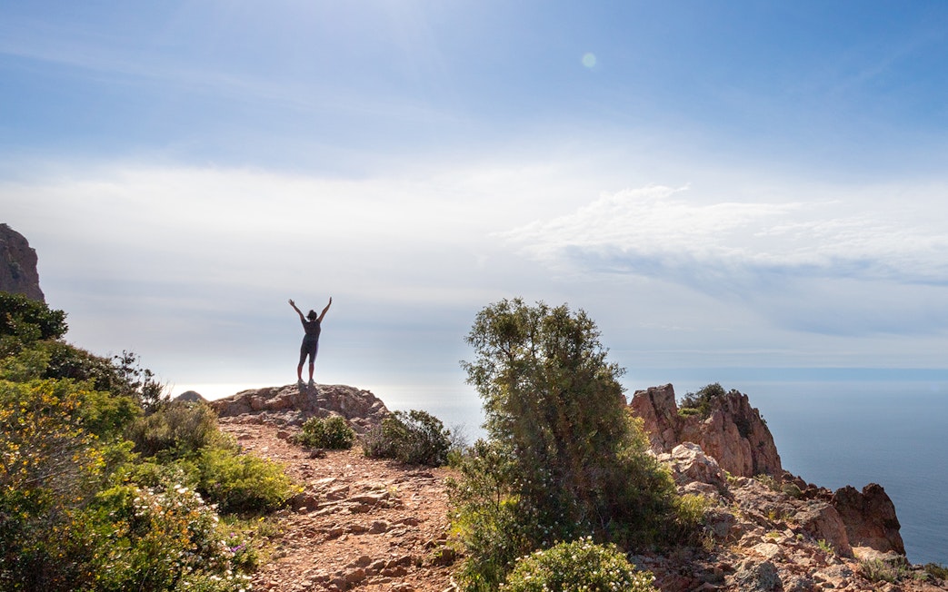 Hiker on rocky cliff overlooking sea at Massif de l'Esterel, France.