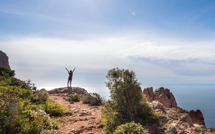 Hiker on rocky cliff overlooking sea at Massif de l'Esterel, France.
