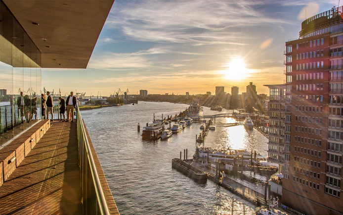 Visitors on Elphi Plaza balcony overlooking HafenCity harbor at sunset, Hamburg.