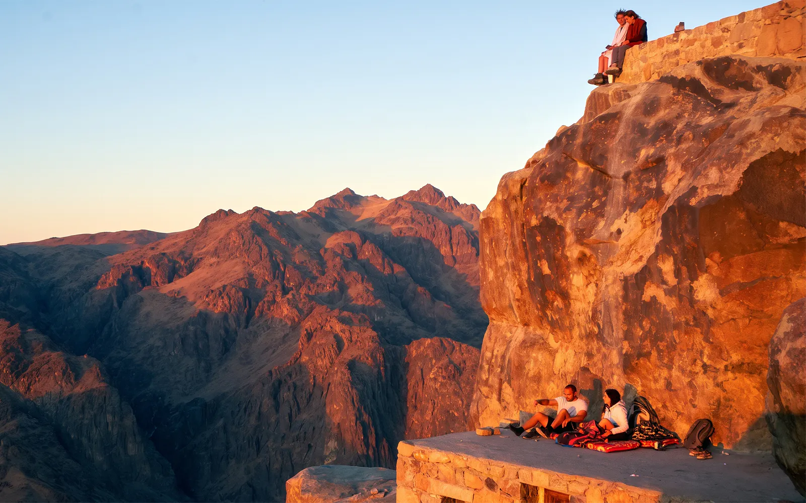Mount Sinai sunrise view with tourists resting on a rocky ledge.