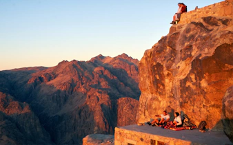 Mount Sinai sunrise view with tourists resting on a rocky ledge.