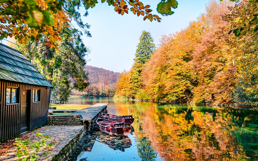 Boats docked on a clear lake surrounded by autumn trees in Plitvice National Park.