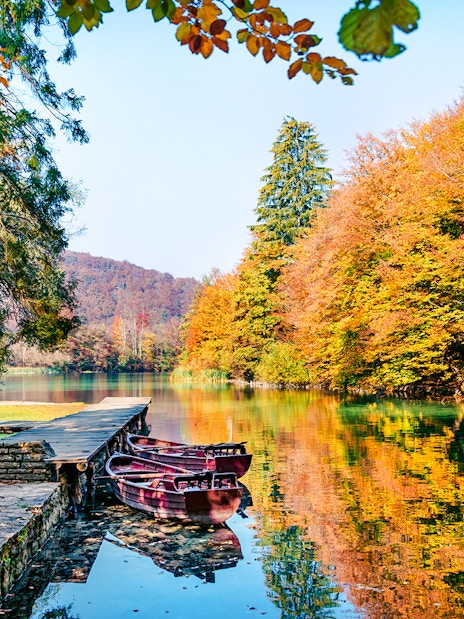 Boats docked on a clear lake surrounded by autumn trees in Plitvice National Park.