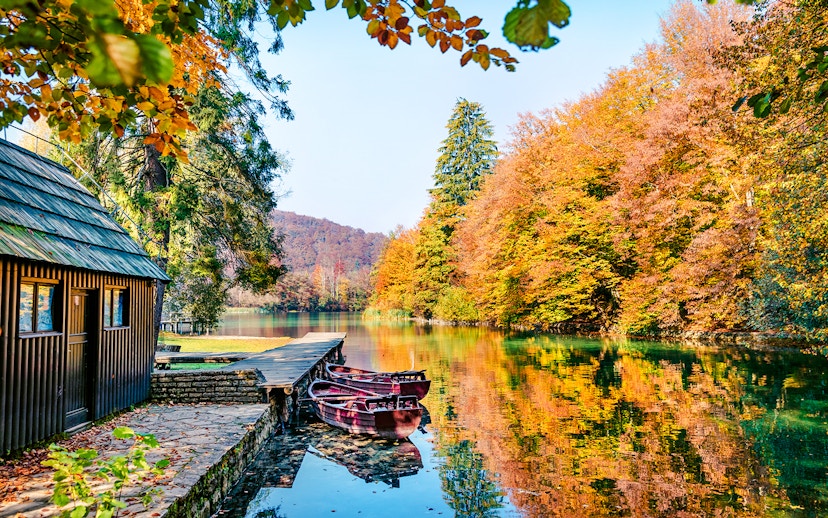 Boats docked on a clear lake surrounded by autumn trees in Plitvice National Park.