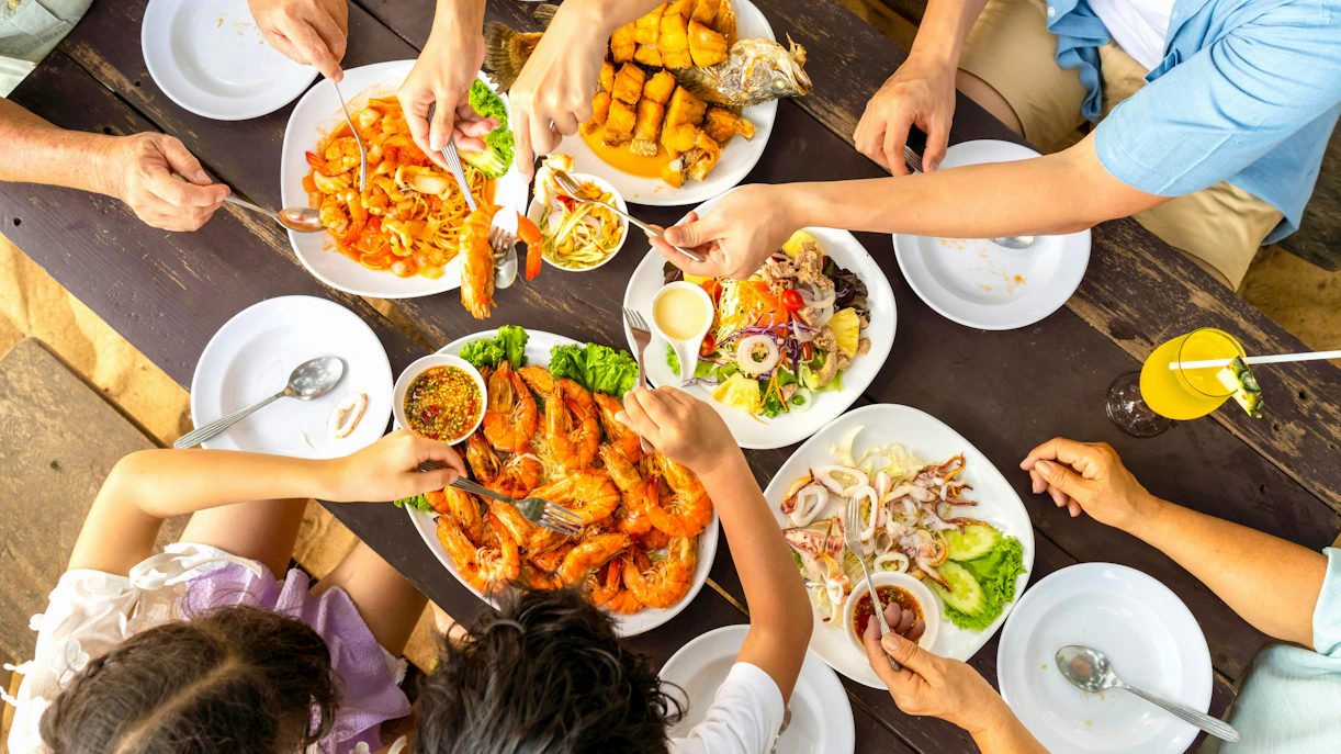 Family enjoying seafood lunch at a beachside table with shrimp and fish dishes.