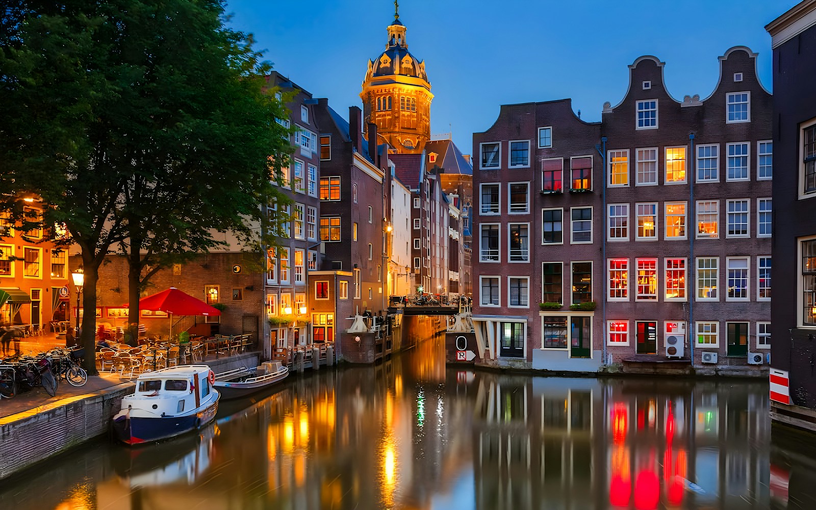 Evening view of Amsterdam canal with illuminated buildings and a boat.