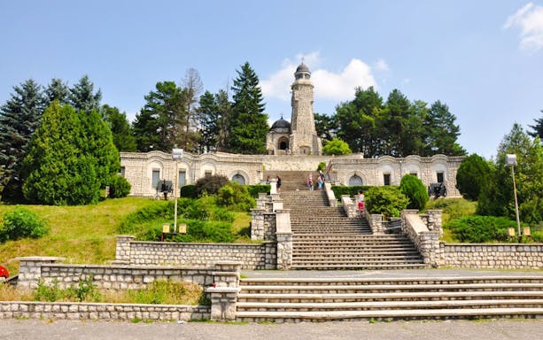 Heroes Mausoleum in Romania with stone steps leading to the monument surrounded by trees.