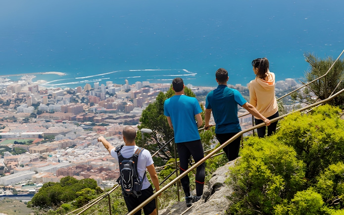 Group hiking on Monte Calamorro with views of the city and sea, Spain.