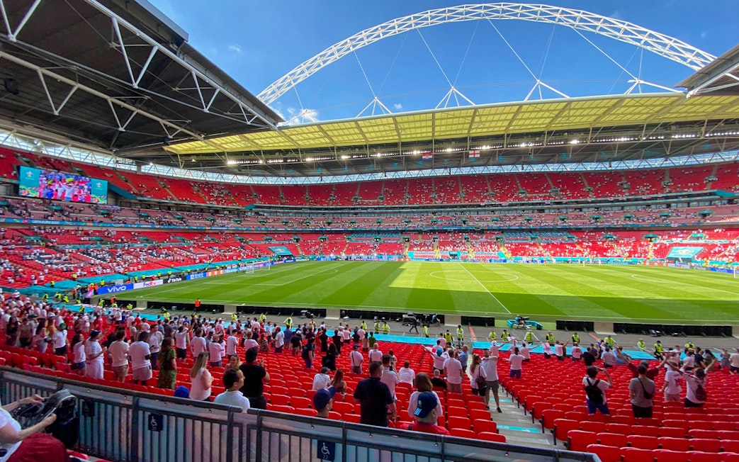 Wembley Stadium interior with spectators and football field during a match.