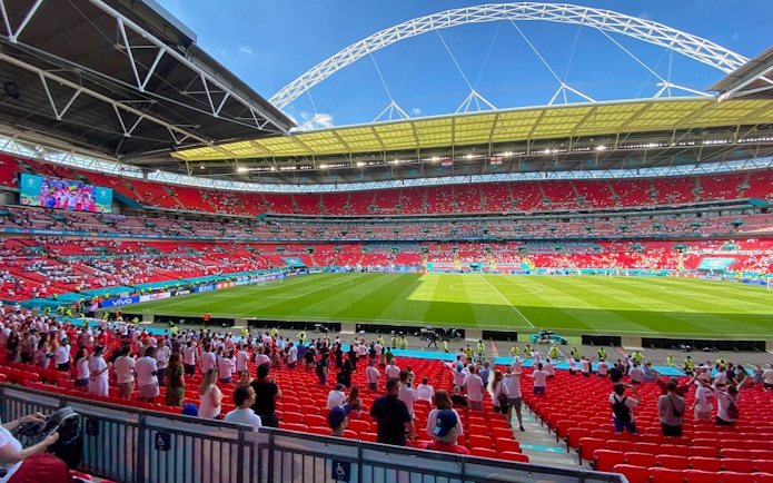 Wembley Stadium interior with spectators and football field during a match.