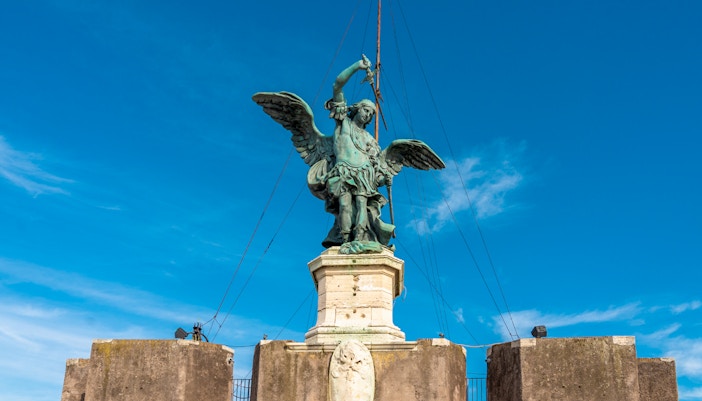 Archangel Michael statue on Castel Sant'Angelo, Rome, under clear blue sky.