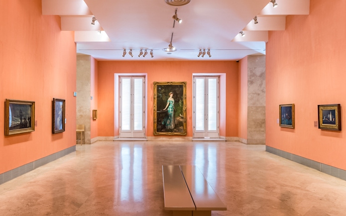 Thyssen Museum gallery with paintings on orange walls in Madrid, Spain.