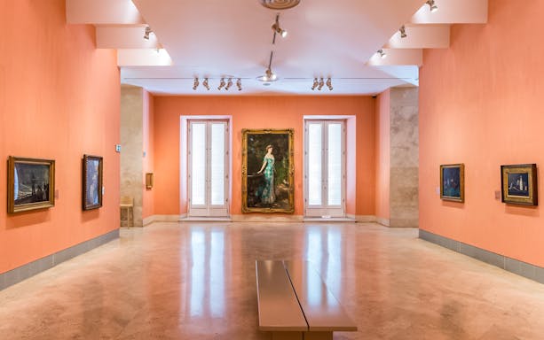 Thyssen Museum gallery with paintings on orange walls in Madrid, Spain.
