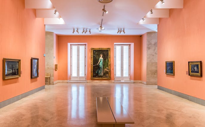 Thyssen Museum gallery with paintings on orange walls in Madrid, Spain.