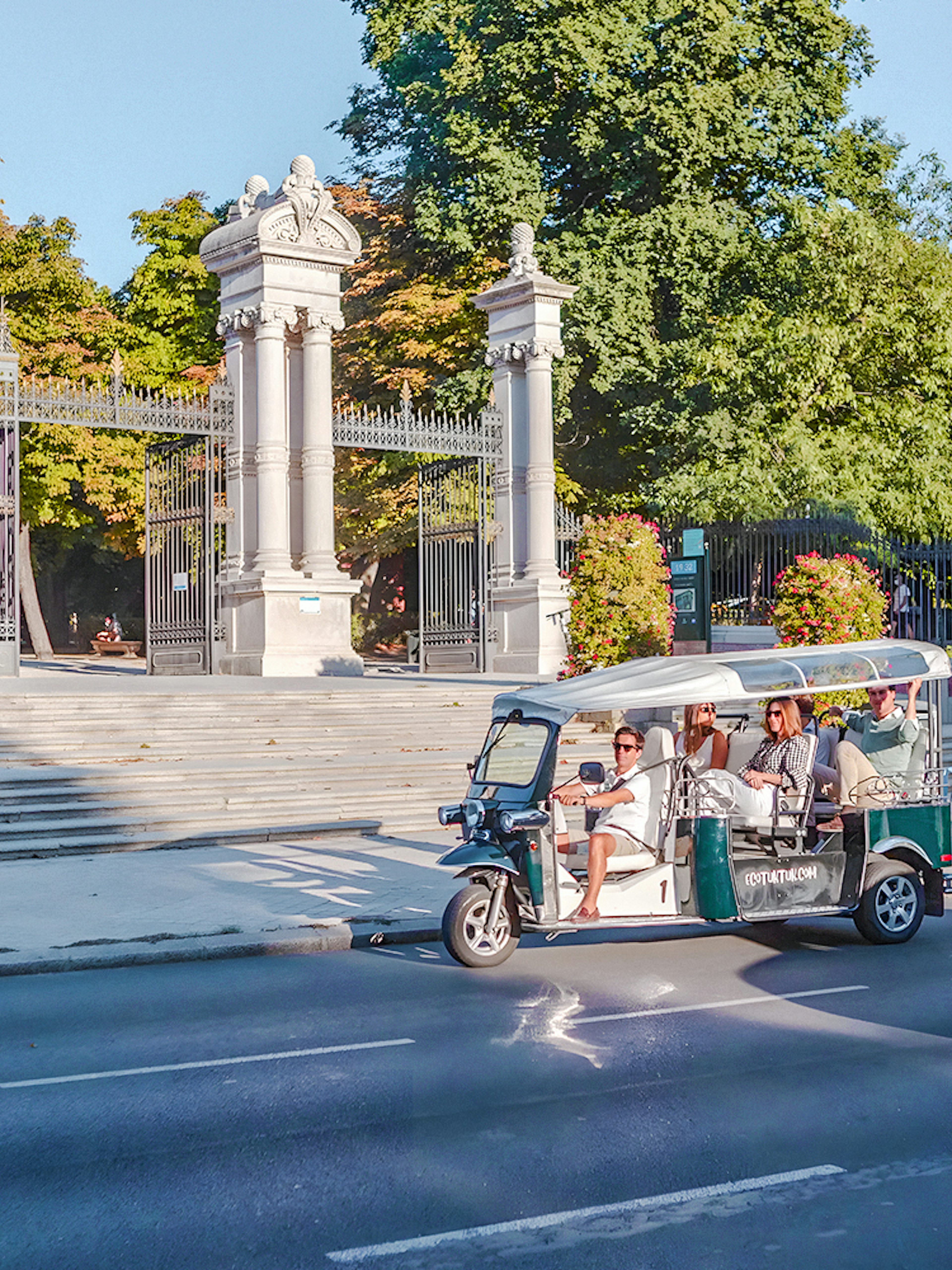 Electric tuk-tuk passing Puerta de España gate in Madrid, Spain.